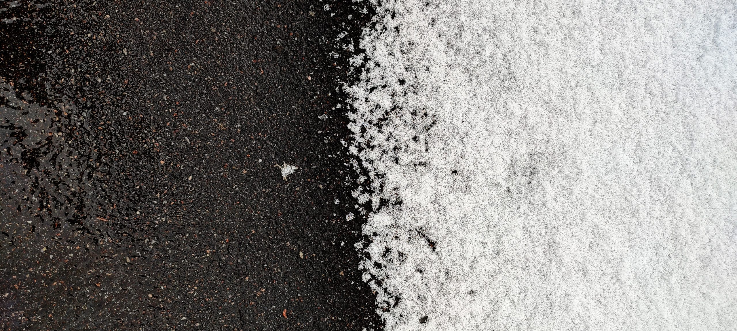 The border of snow and asphalt. Winter Asphalt Maintenance A close-up of a snow-dusted black asphalt surface, half covered in white snow, creating a stark contrast.