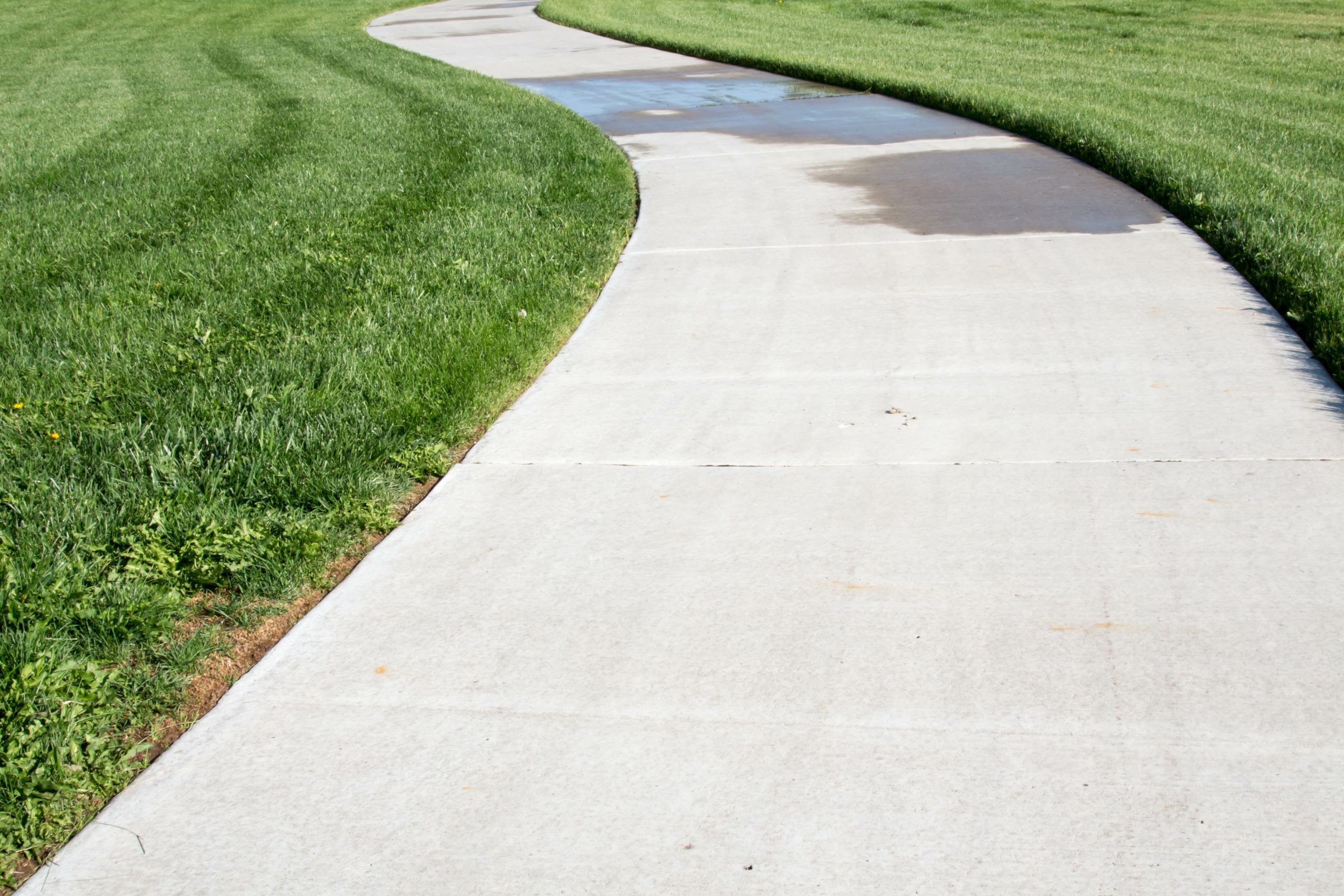 Curving concrete sidewalk through green grass Professional Walkway Paving Curved concrete pathway bordered by freshly mowed green grass in sunlight.