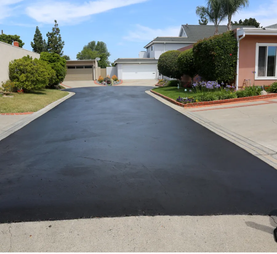 Freshly paved black driveway leading to a residential garage, with houses and gardens on either side.