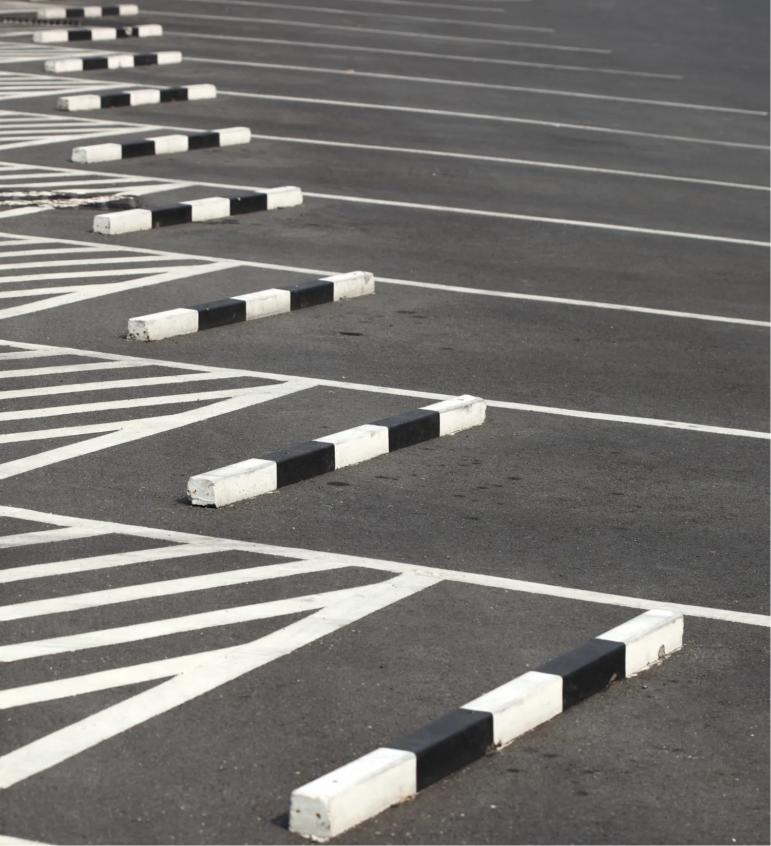 parking-lot-4 Empty parking lot with black and white striped barriers and designated parking lines on an asphalt surface.