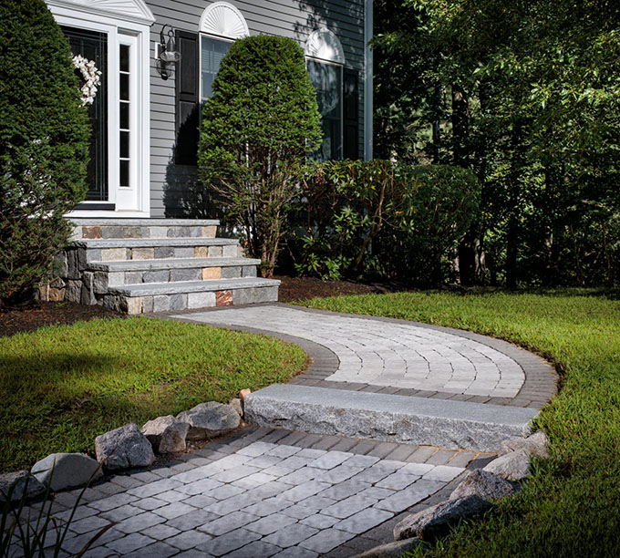Inspiration_Walkways_Image20 Curved stone walkway leading to front steps of a house, bordered by grass and shrubs.