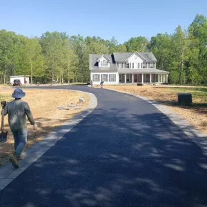 A newly paved driveway leads to a large house surrounded by trees, with a person walking on the left.