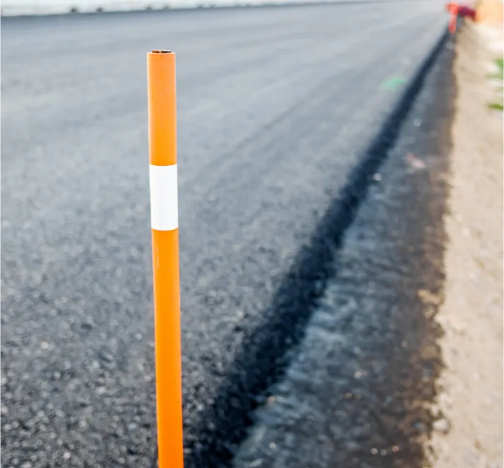 overlays-2 Orange road marker post on the edge of a newly paved asphalt road with blurred background.