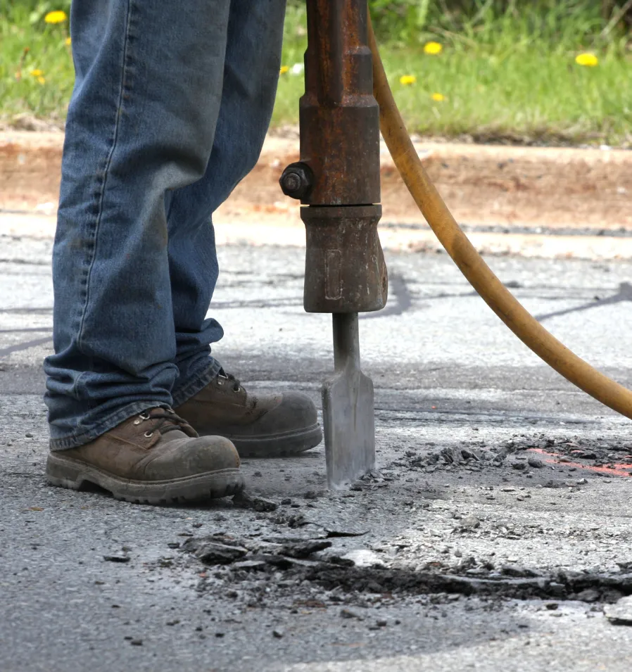 repair-2 Person using a jackhammer to break up pavement on a road, wearing jeans and work boots.