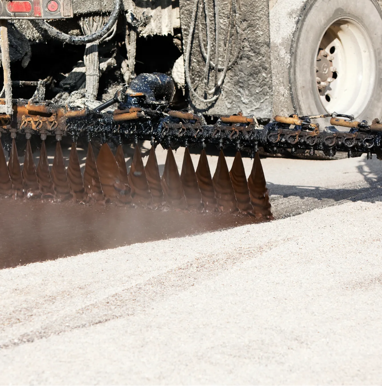 tar-and-chip-1 Close-up of a machine spreading asphalt or tar during a road construction or resurfacing process.