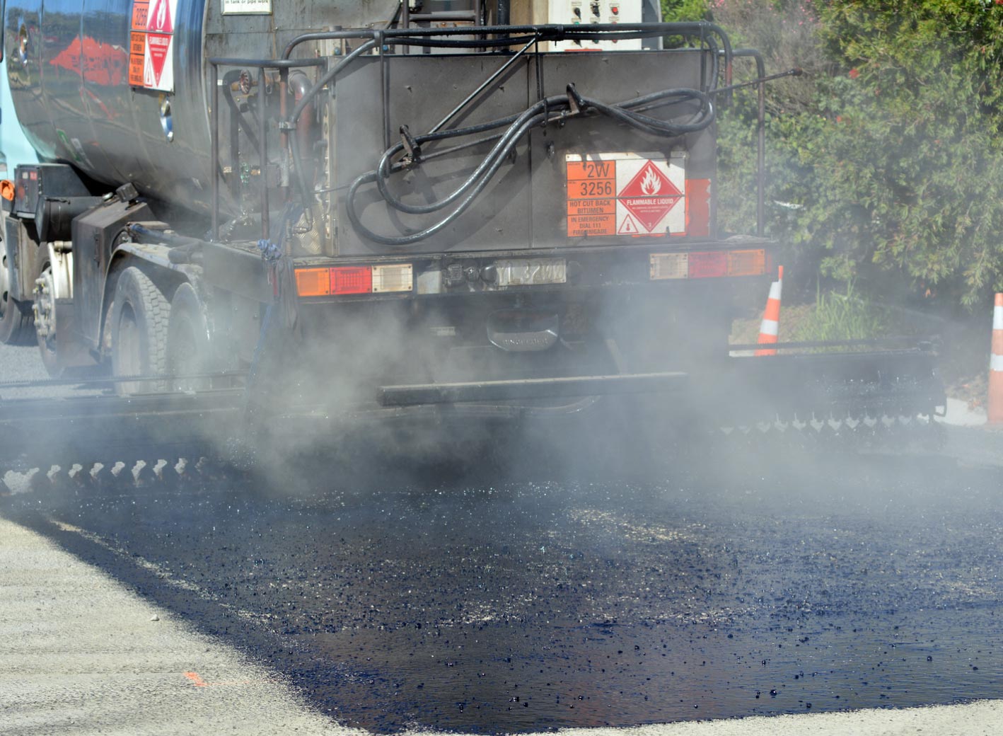 tar-img A truck spreads hot asphalt on a road, with steam rising and traffic cones visible in the background.