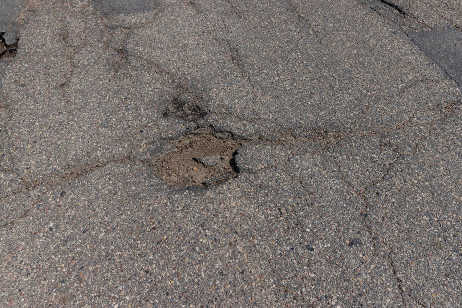 A pothole in cracked asphalt pavement on a road surface.